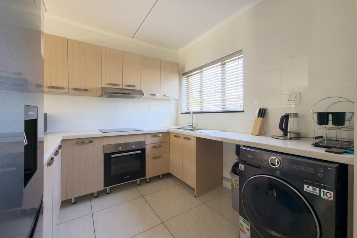 A functional kitchen featuring light wood cabinetry, a built-in oven, electric hob, extractor fan, and tiled flooring with space for a washing machine.