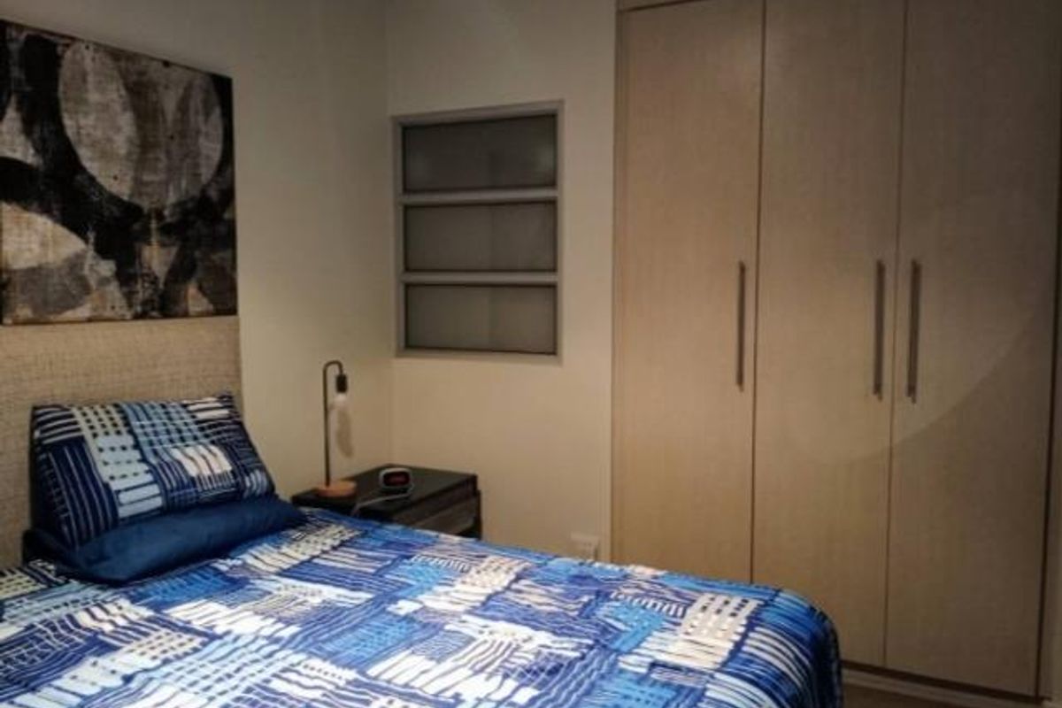A bedroom featuring a built-in wardrobe with light wood-finish doors and a louver-style window providing natural light.