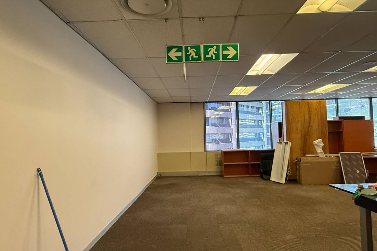 An open-plan office space featuring a suspended ceiling with recessed lighting, large windows, and carpeted flooring, currently in need of refurbishment.