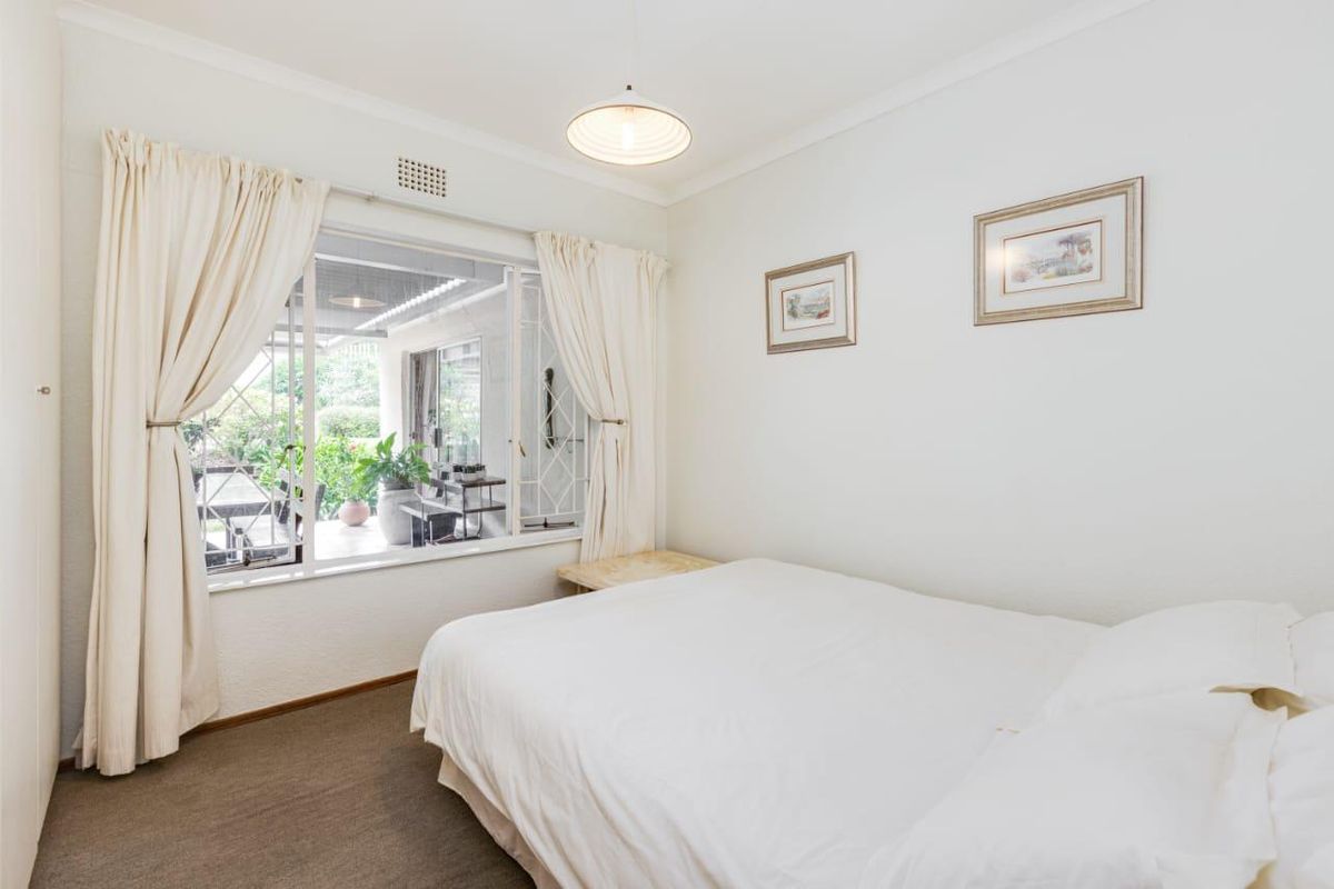 A bright bedroom featuring carpeted flooring, built-in cupboards, and a large window providing views of the outdoor patio area.