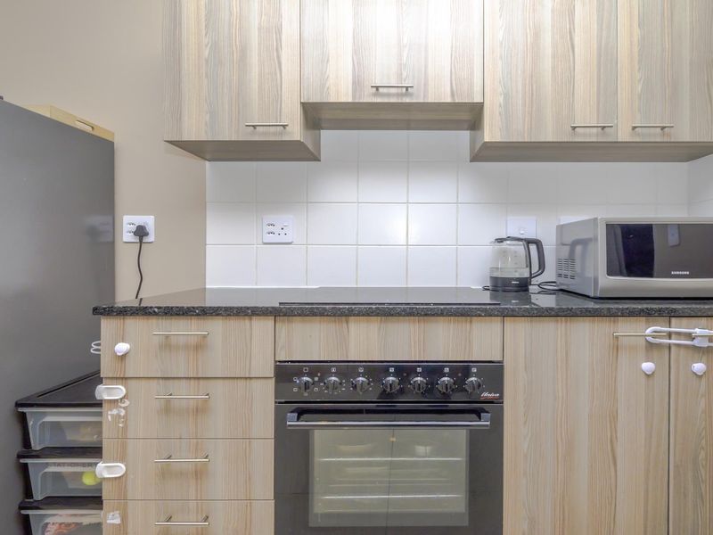 A functional kitchen featuring wood-look cabinetry, granite countertops, a white tiled backsplash, and a built-in oven with an electric hob.