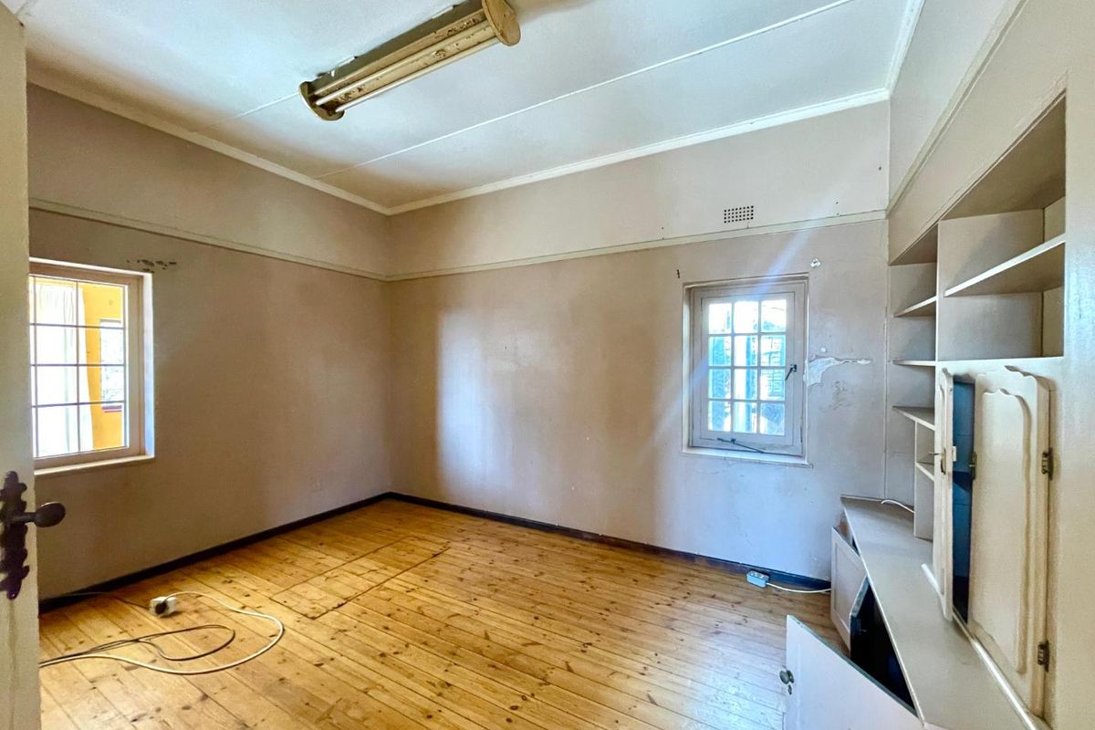 An empty bedroom featuring original timber flooring, built-in shelving, and timber-framed windows, requiring cosmetic updates and wall repairs.