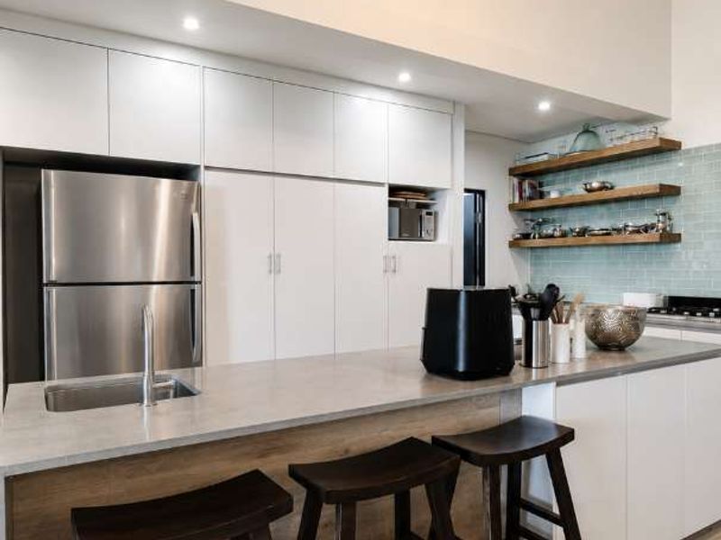 Modern kitchen featuring sleek white cabinetry, stone countertops, floating timber shelving, and stylish pendant lighting, creating a bright and functional culinary space.