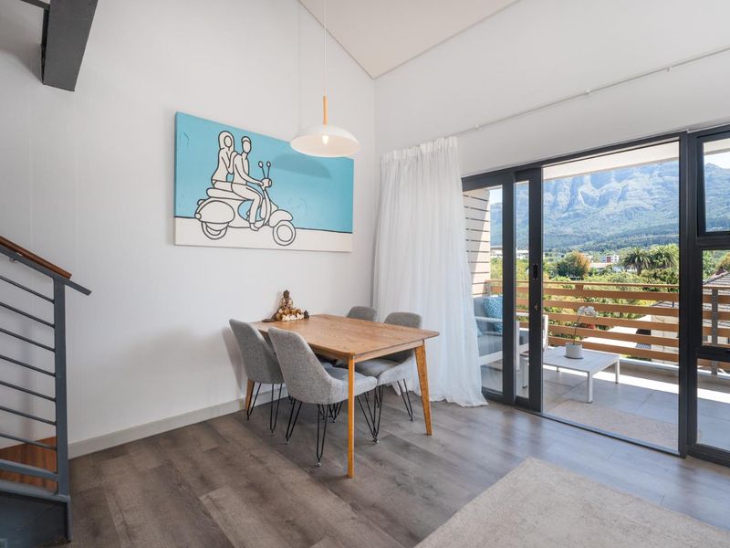Bright living area featuring modern laminate flooring, a sleek staircase, and large sliding doors opening onto a balcony with scenic mountain views.