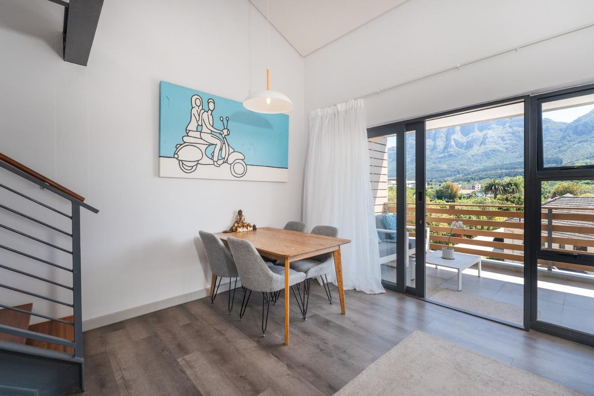 Bright living area featuring modern laminate flooring, a sleek staircase, and large sliding doors opening onto a balcony with scenic mountain views.