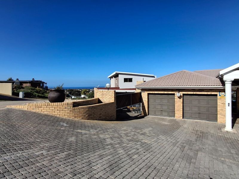 Front exterior view featuring a paved driveway, double garage, and a brick retaining wall with a view of the surrounding area.