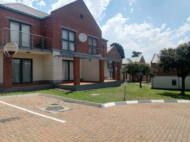 Exterior view of a brick apartment complex featuring covered ground-floor patios, upper-level balconies, and a paved driveway area.