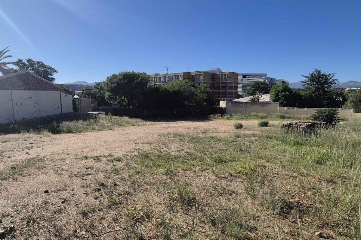 A vacant residential plot featuring a level terrain, perimeter boundary walls, and established surrounding vegetation in an urban setting.