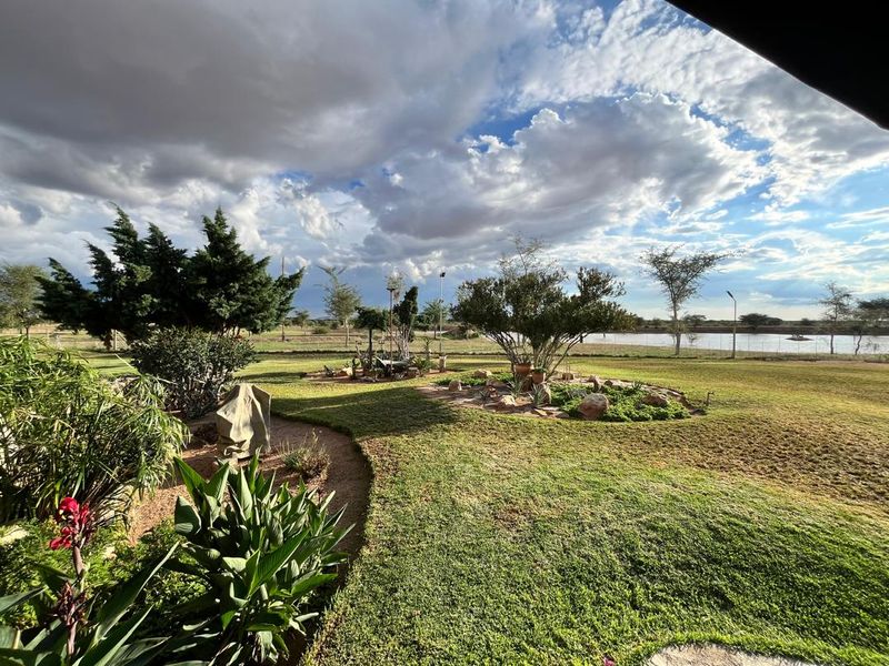 A well-maintained farm garden featuring expansive lawns, established trees, and landscaped rock beds with a scenic view of the surrounding landscape.