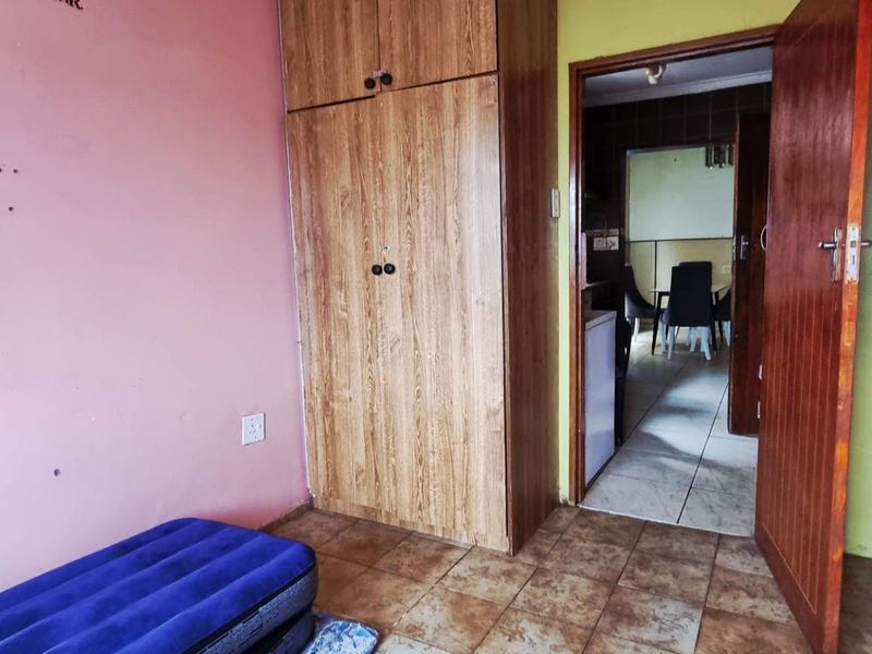 A bedroom featuring tiled flooring and a built-in wooden wardrobe, with direct access to an adjacent living area.