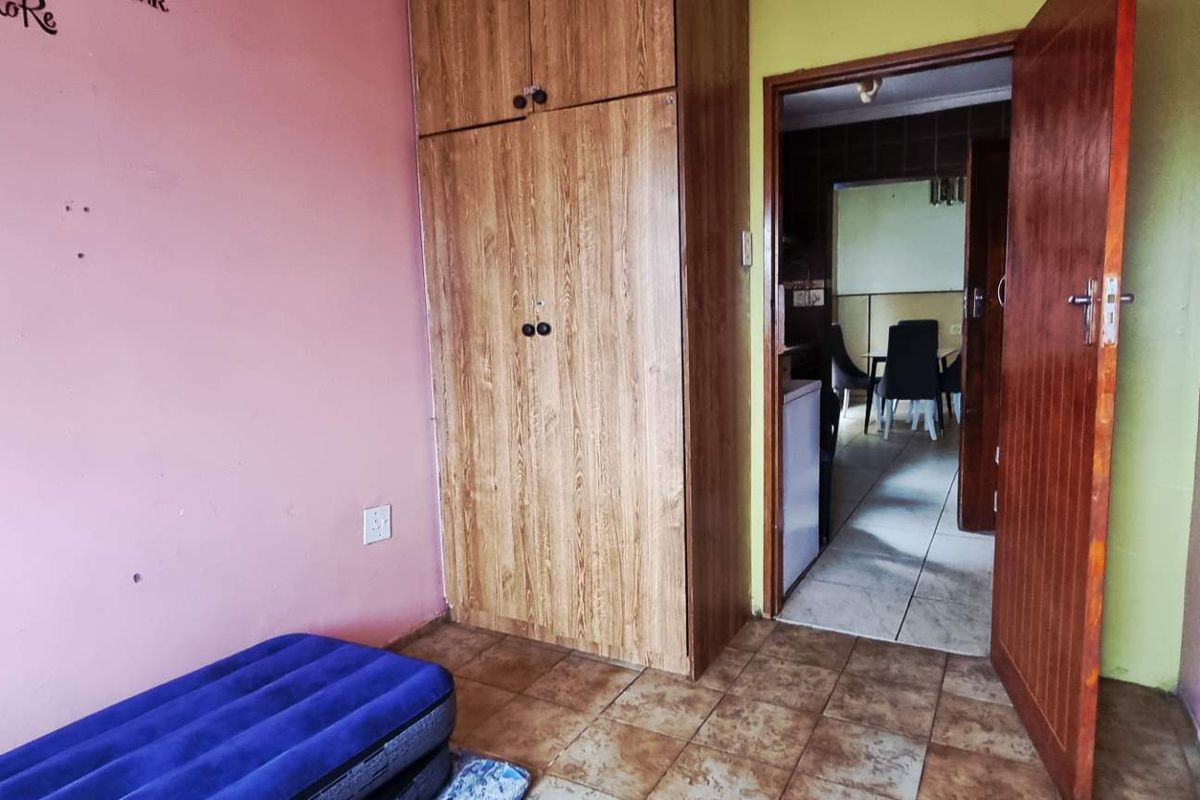 A bedroom featuring tiled flooring and a built-in wooden wardrobe, with direct access to an adjacent living area.
