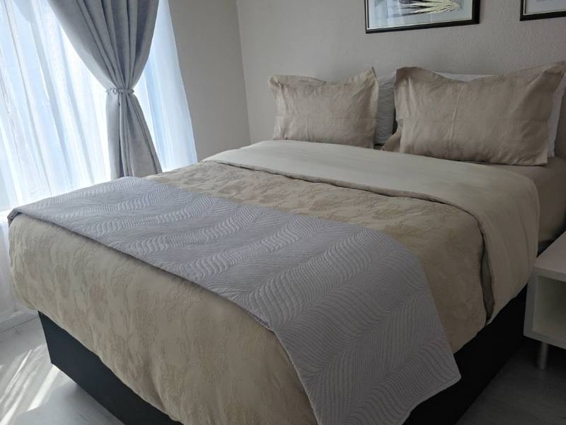 A well-maintained bedroom featuring light-toned laminate flooring and natural light filtering through window curtains.