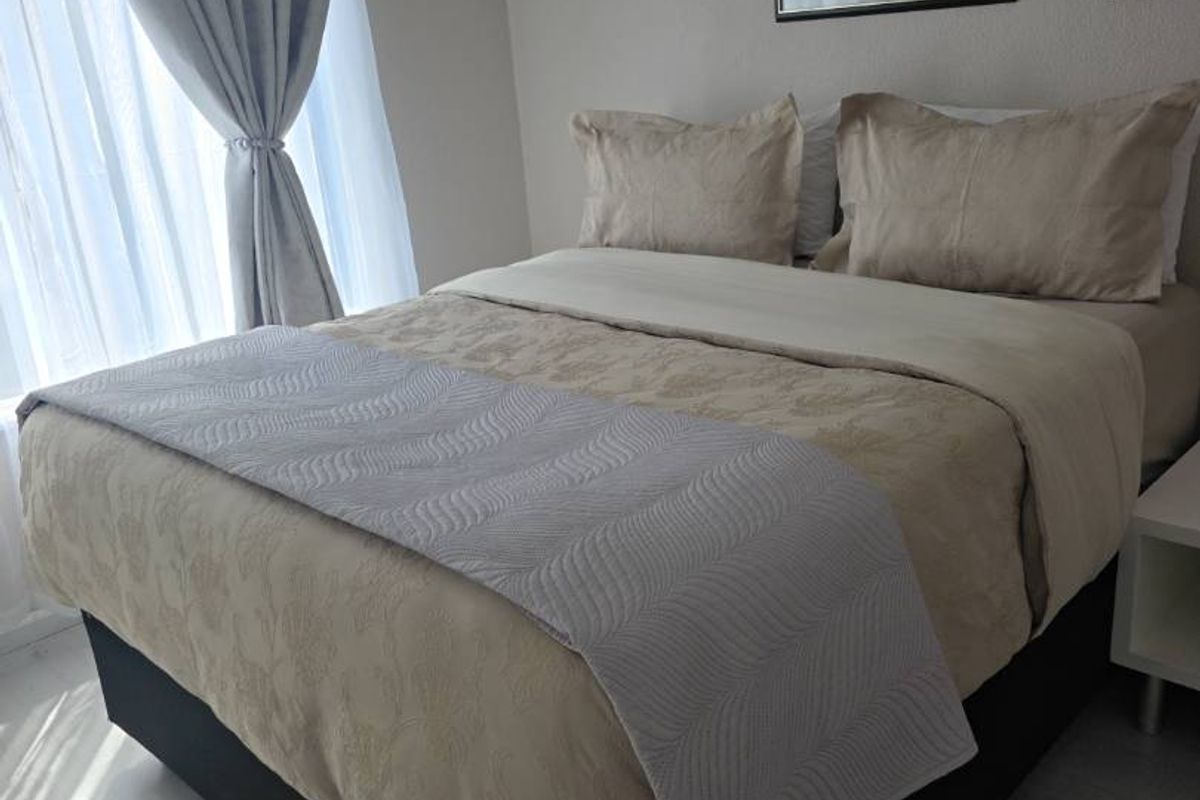 A well-maintained bedroom featuring light-toned laminate flooring and natural light filtering through window curtains.