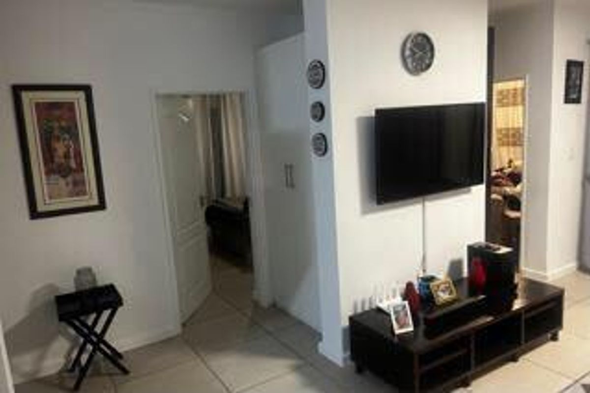 A view of the living area featuring tiled flooring, a wall-mounted television, and access to an adjacent room.