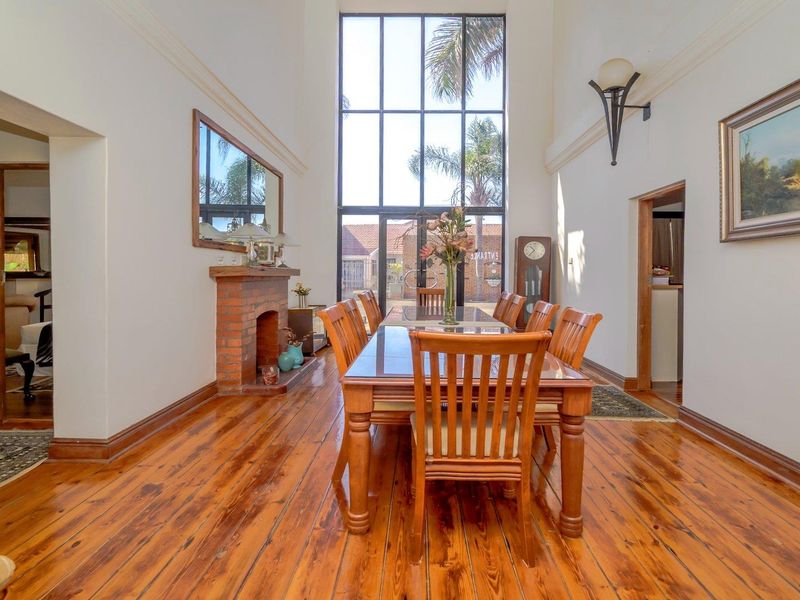 Spacious dining room featuring polished hardwood floors, a classic brick fireplace, and impressive double-height windows that provide abundant natural light.
