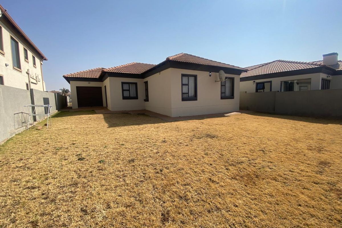 Rear view of the house featuring a tiled roof, neutral exterior walls, and a private backyard with boundary walling.
