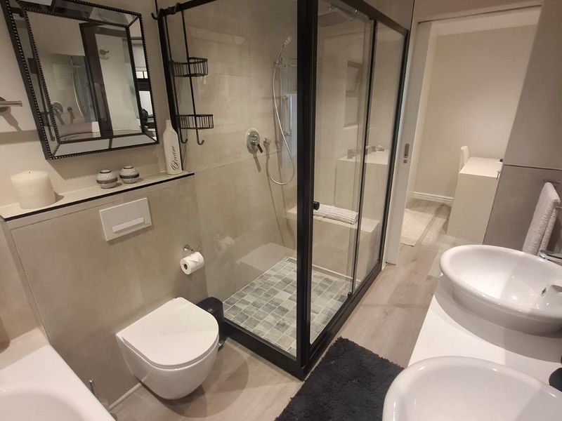 Modern bathroom featuring a double vanity, wall-hung toilet with concealed cistern, and a spacious glass-enclosed shower with contemporary tiling.