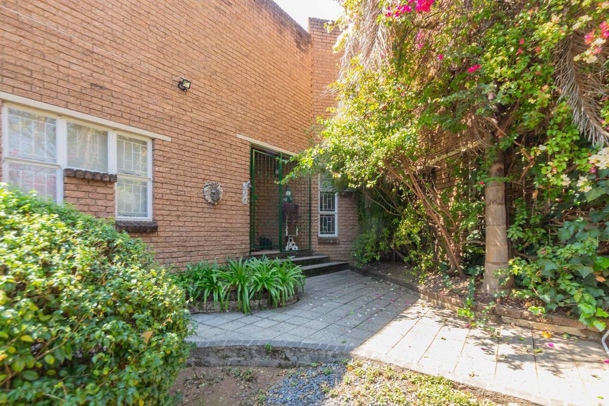 A rear exterior view featuring a brick facade, a paved patio area, and established garden landscaping with security features on windows and doors.