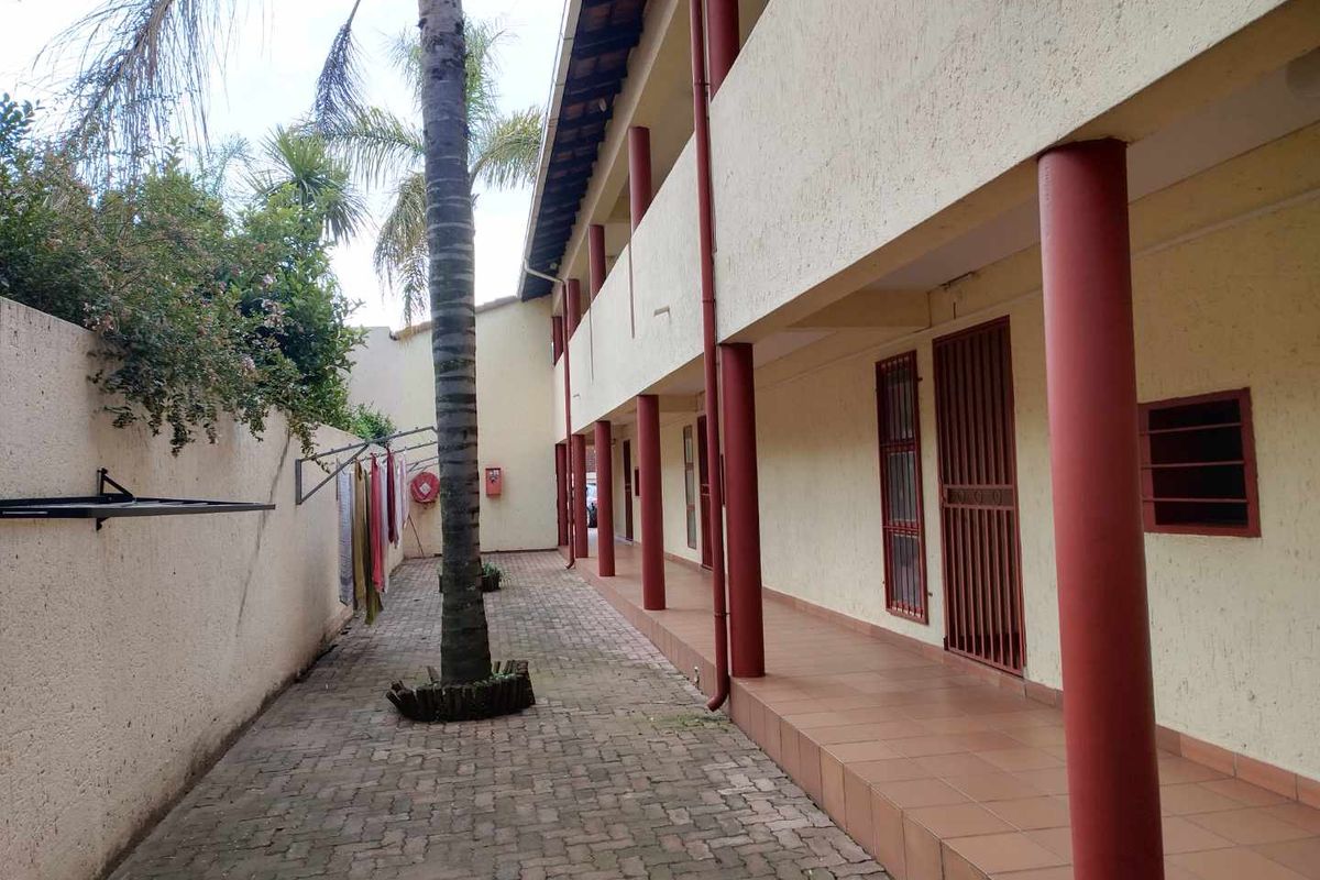 A view of the apartment complex exterior featuring a paved walkway, covered corridor, and security gates along the building facade.