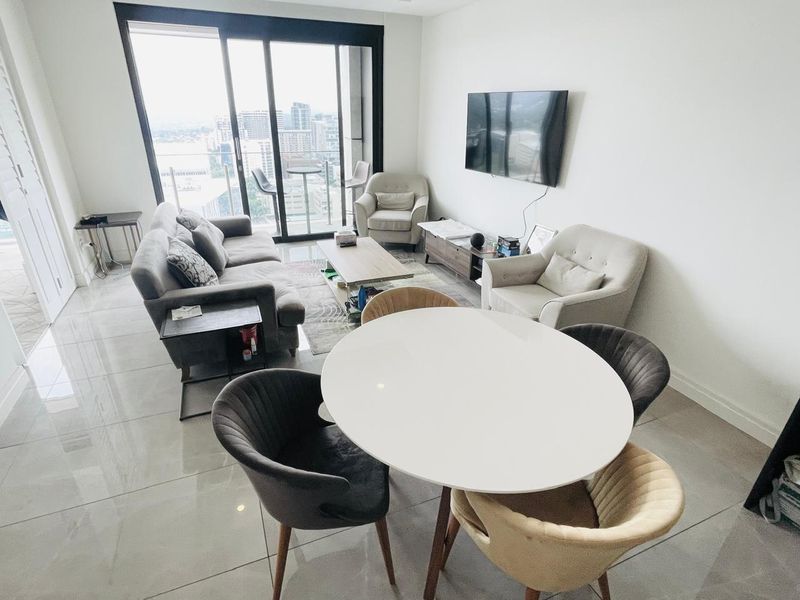 Bright open-plan living and dining area featuring large sliding glass doors leading to a balcony with city views and modern tiled flooring.
