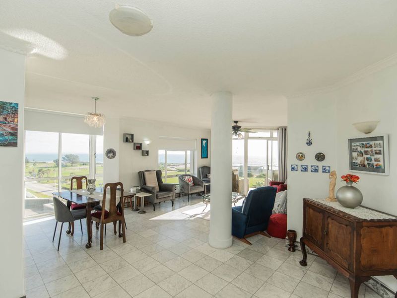 Spacious open-plan living and dining area featuring tiled flooring, a central structural column, and large sliding glass doors with scenic coastal views.