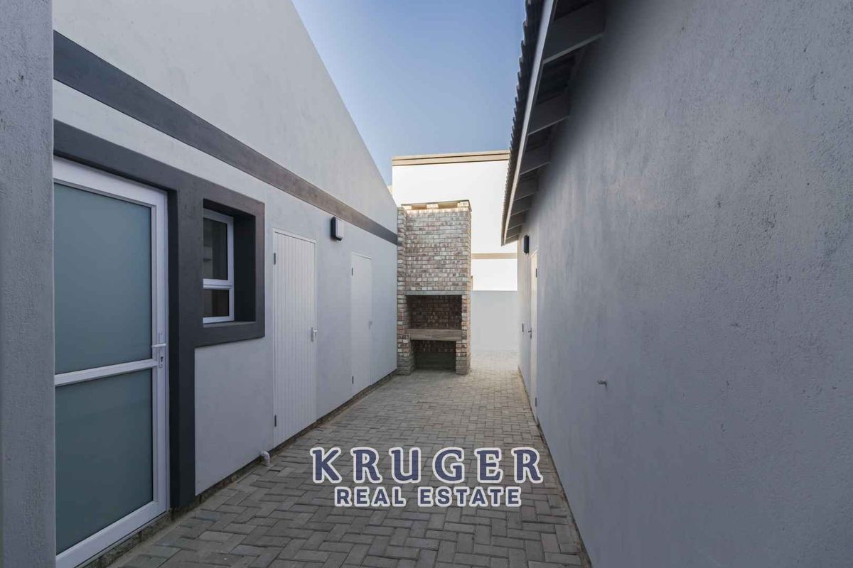 A paved outdoor courtyard area featuring a built-in brick braai or barbecue fireplace, situated between two sections of the property.