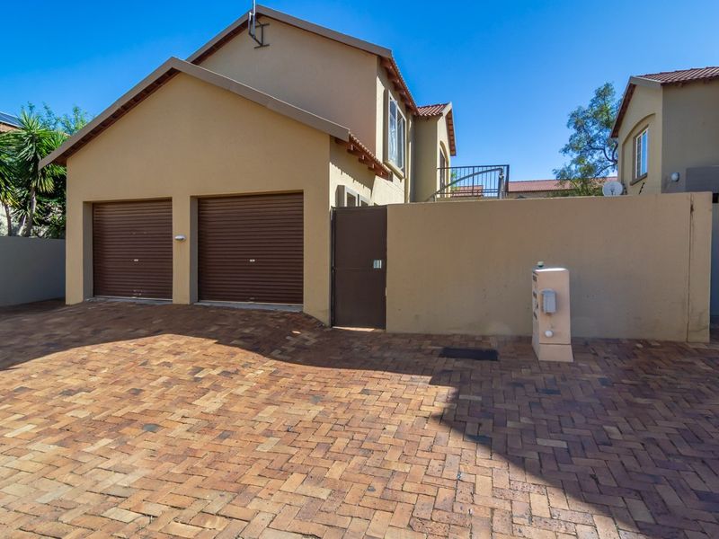 Front view of the townhouse featuring a double garage with roll-up doors, a paved driveway, and a secure pedestrian gate.