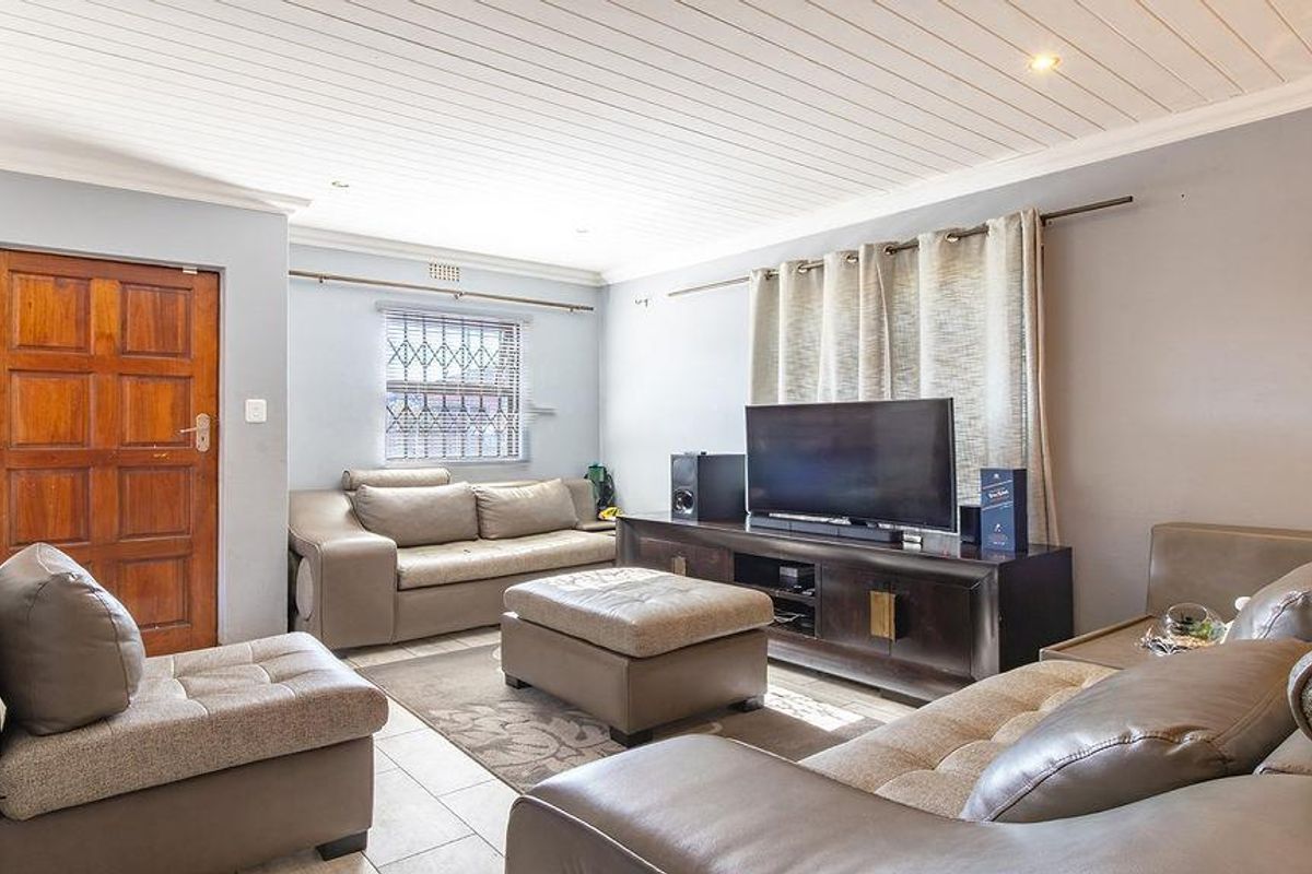 A comfortable living room featuring tiled flooring, a timber panelled ceiling, and security bars on the window.