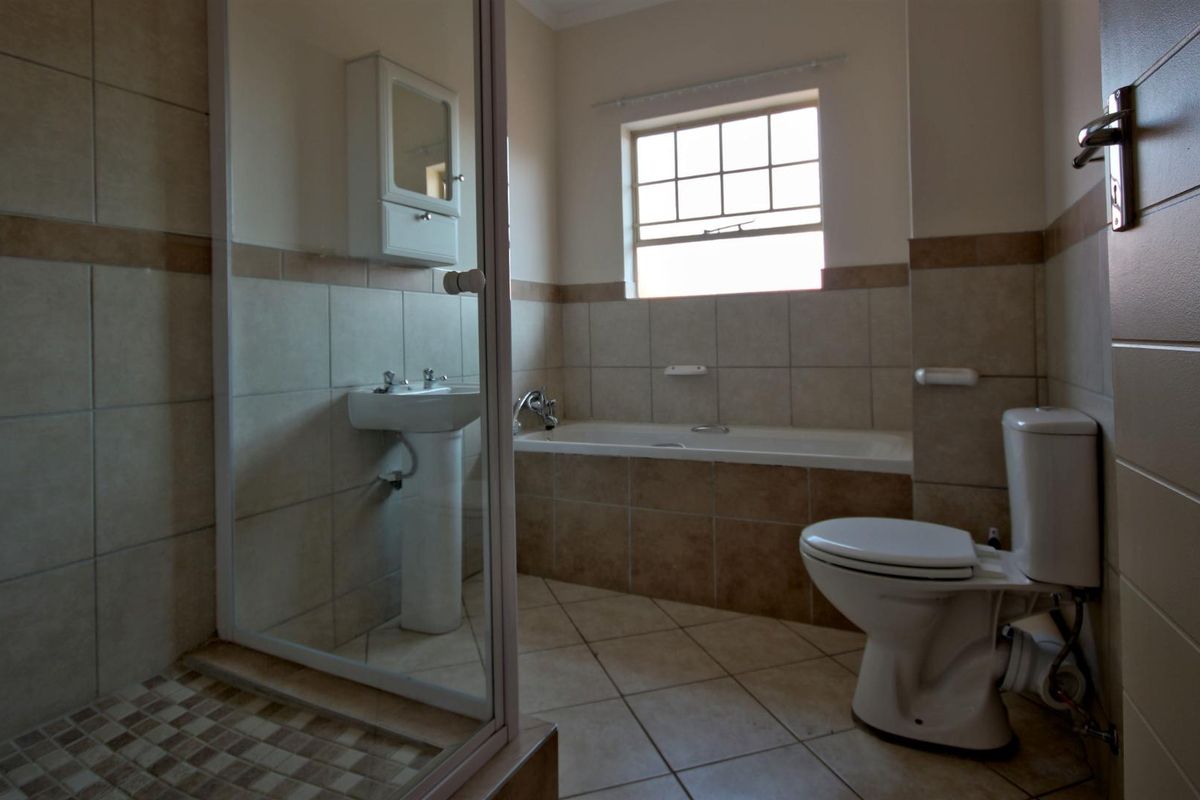 A functional bathroom featuring a pedestal basin, built-in bathtub, separate shower enclosure, and toilet with neutral tiled finishes.
