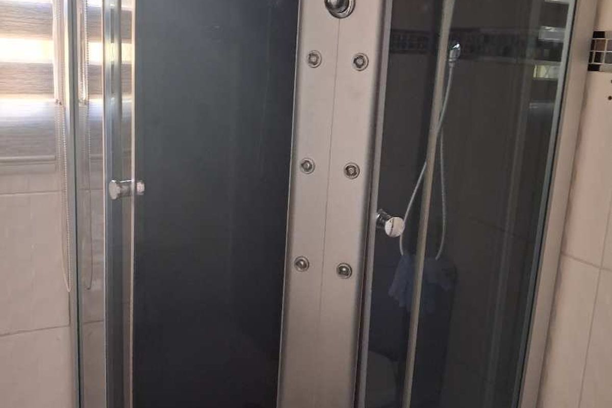 A corner shower unit featuring a built-in hydro-massage panel, glass enclosure, and tiled wall surrounds.