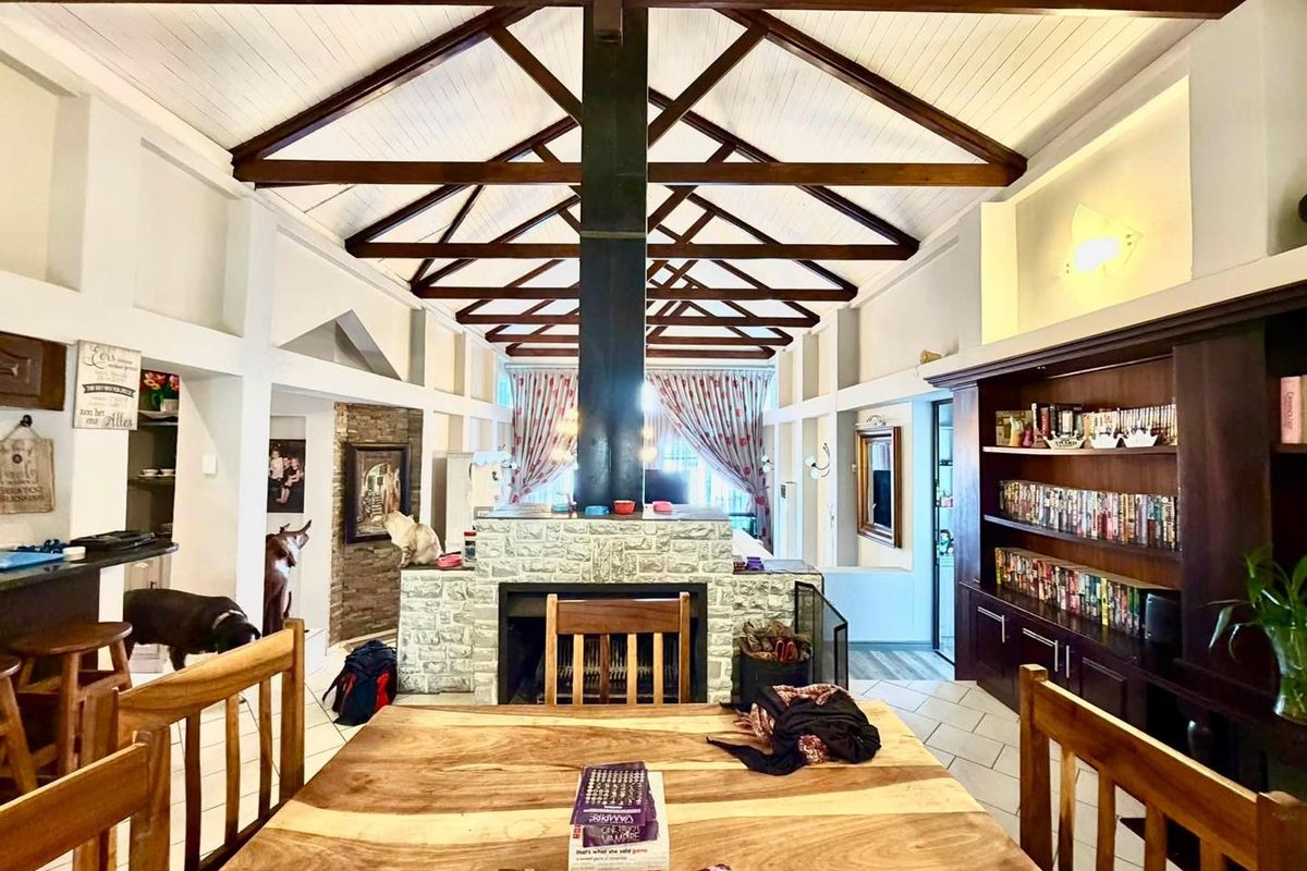 Spacious living area featuring high vaulted ceilings with exposed timber trusses, a central stone-clad fireplace, and extensive built-in wooden shelving.