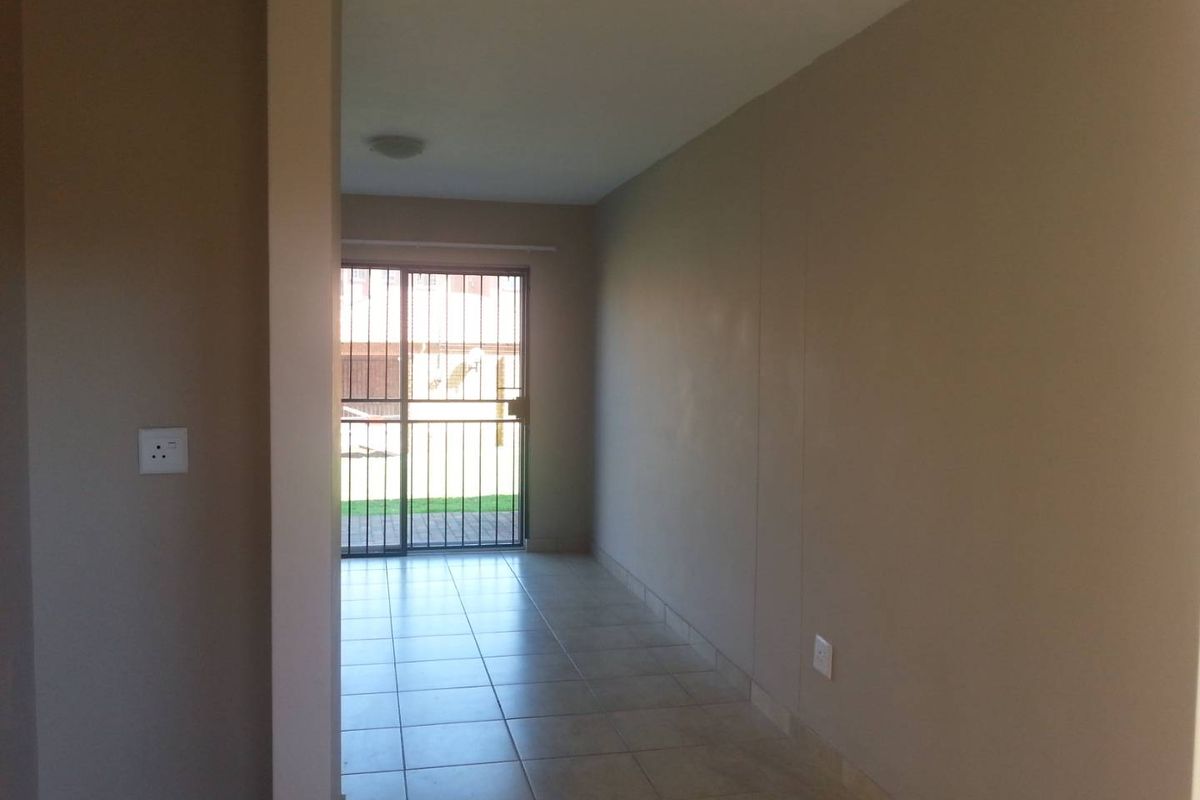 An empty interior living space featuring neutral tiled flooring and a sliding glass door with security gate leading to an outdoor area.
