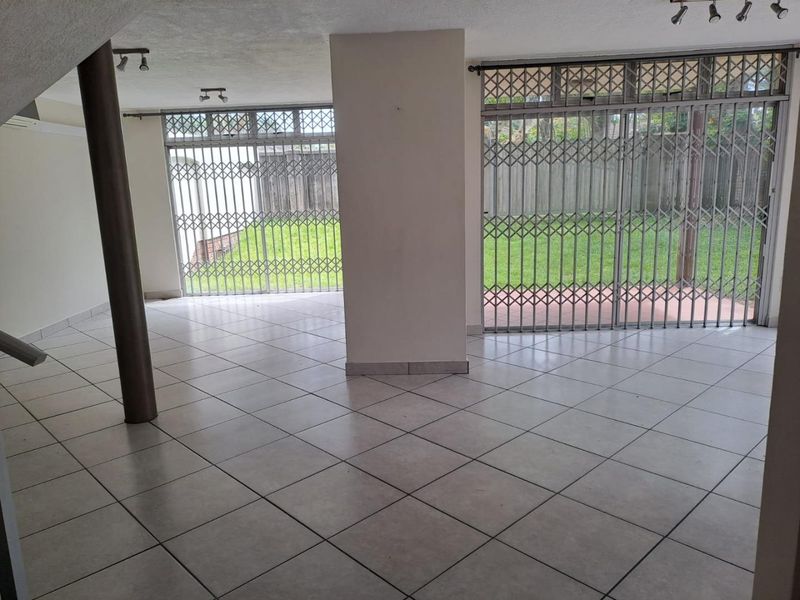 Spacious, empty living area featuring neutral ceramic floor tiles, structural columns, and large sliding glass doors with security gates leading to the rear garden.