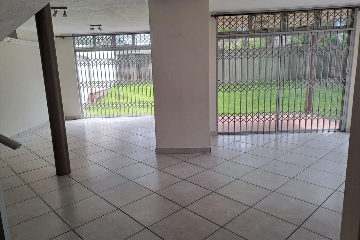 Spacious, empty living area featuring neutral ceramic floor tiles, structural columns, and large sliding glass doors with security gates leading to the rear garden.