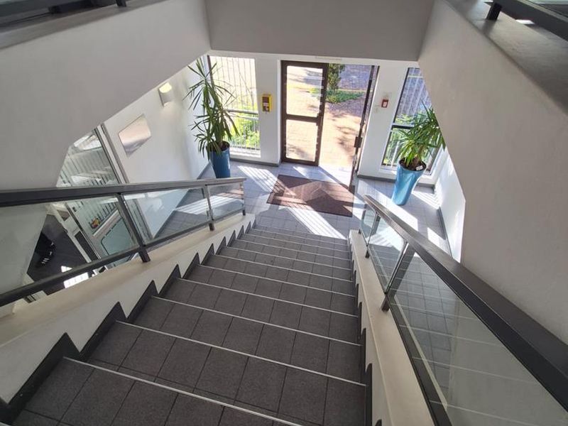 A bright and modern office building entrance featuring a tiled staircase, glass balustrades, and a large overhead skylight providing natural illumination.