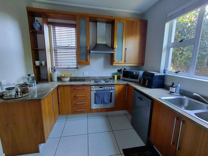 A functional kitchen featuring wooden cabinetry, stone countertops, built-in oven with extractor fan, and tiled flooring, offering a practical layout for daily use.