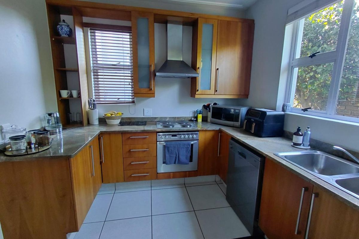 A functional kitchen featuring wooden cabinetry, stone countertops, built-in oven with extractor fan, and tiled flooring, offering a practical layout for daily use.
