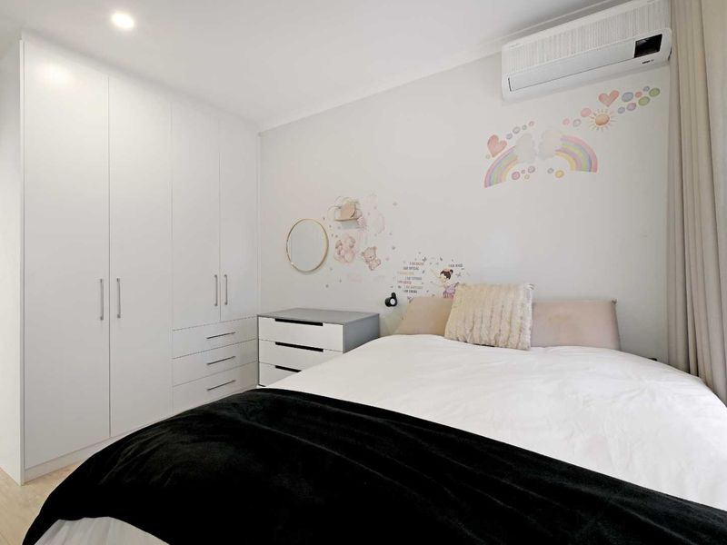 A bright bedroom featuring built-in wardrobes, a split-system air conditioner, and neutral finishes, providing a clean and functional living space.