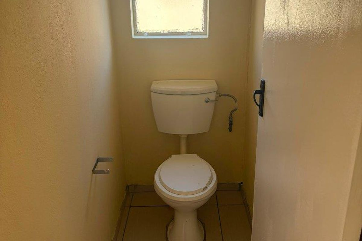 A small, functional guest toilet featuring tiled flooring and a window, currently in need of minor cosmetic updates and finishing touches.