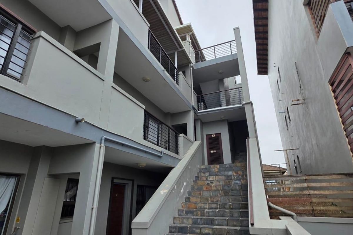 Exterior view of an apartment complex featuring a stone-clad staircase, multi-level balconies with metal railings, and concrete building facade.
