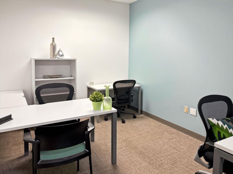 A functional office space featuring neutral carpet flooring, a light blue accent wall, and integrated electrical and data connectivity points.