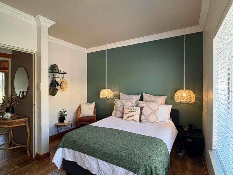 A well-maintained bedroom featuring hardwood flooring, crown molding, and a feature wall with pendant lighting and venetian blinds.