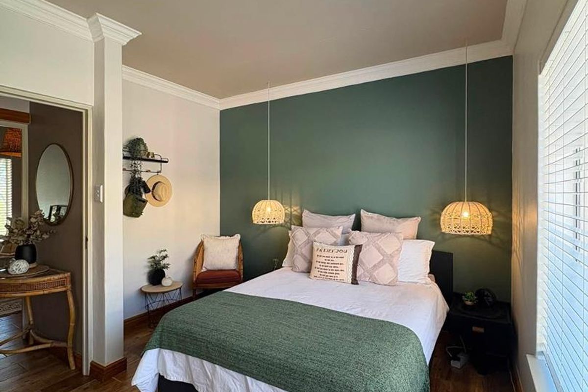 A well-maintained bedroom featuring hardwood flooring, crown molding, and a feature wall with pendant lighting and venetian blinds.