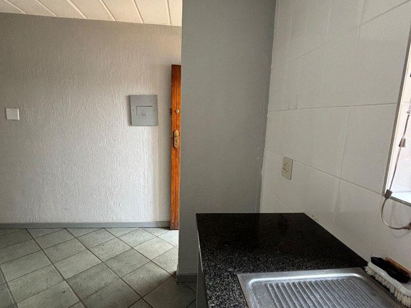 A functional kitchen area featuring granite countertops, a stainless steel sink, and tiled flooring, presenting an opportunity for cosmetic updates.