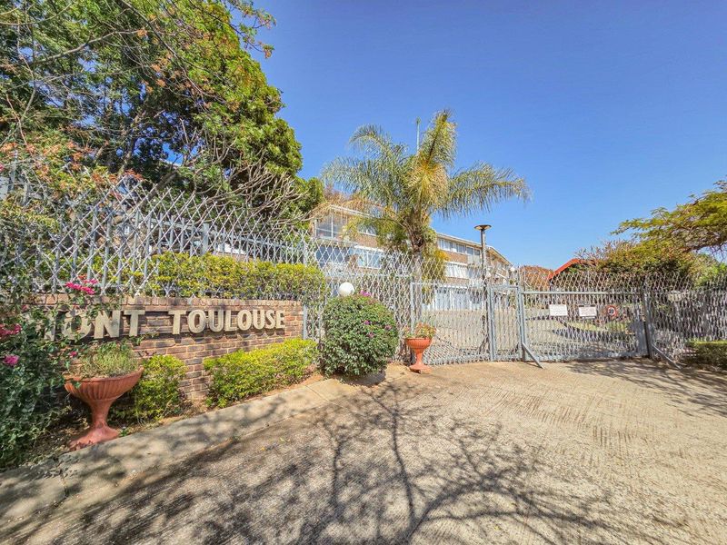 Front entrance view of the Mont Toulouse apartment complex featuring a brick boundary wall, security fencing, and a gated driveway access point.