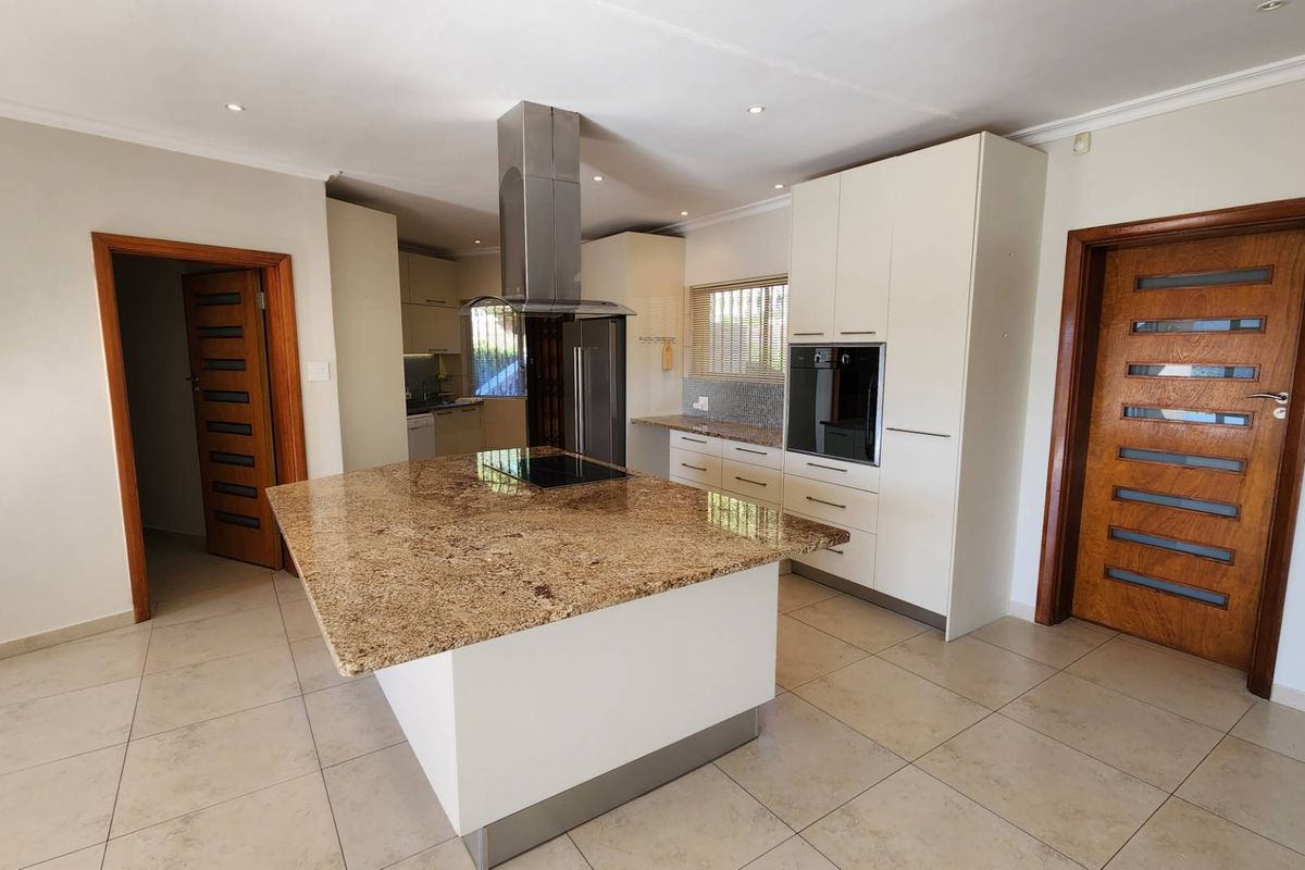 Modern kitchen featuring a large granite island, built-in oven, extractor fan, and ample cabinetry, finished with neutral tiled flooring and recessed lighting.