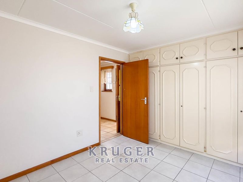 A bright, empty bedroom featuring neutral tiled flooring and extensive built-in cupboard storage, offering a clean and versatile space.
