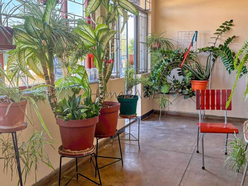 A sunlit enclosed patio or sunroom featuring large windows with security bars and durable tiled flooring, offering a bright and versatile space.