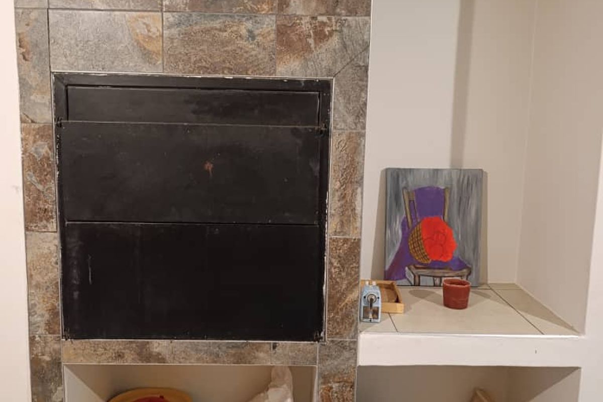 A built-in indoor braai fireplace featuring stone-look tile cladding and adjacent storage shelving, suitable for entertaining.