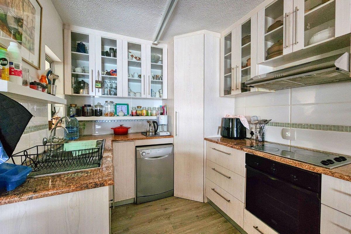 Functional kitchen featuring light-toned cabinetry, granite-look countertops, built-in oven, electric hob, and an integrated extractor fan.